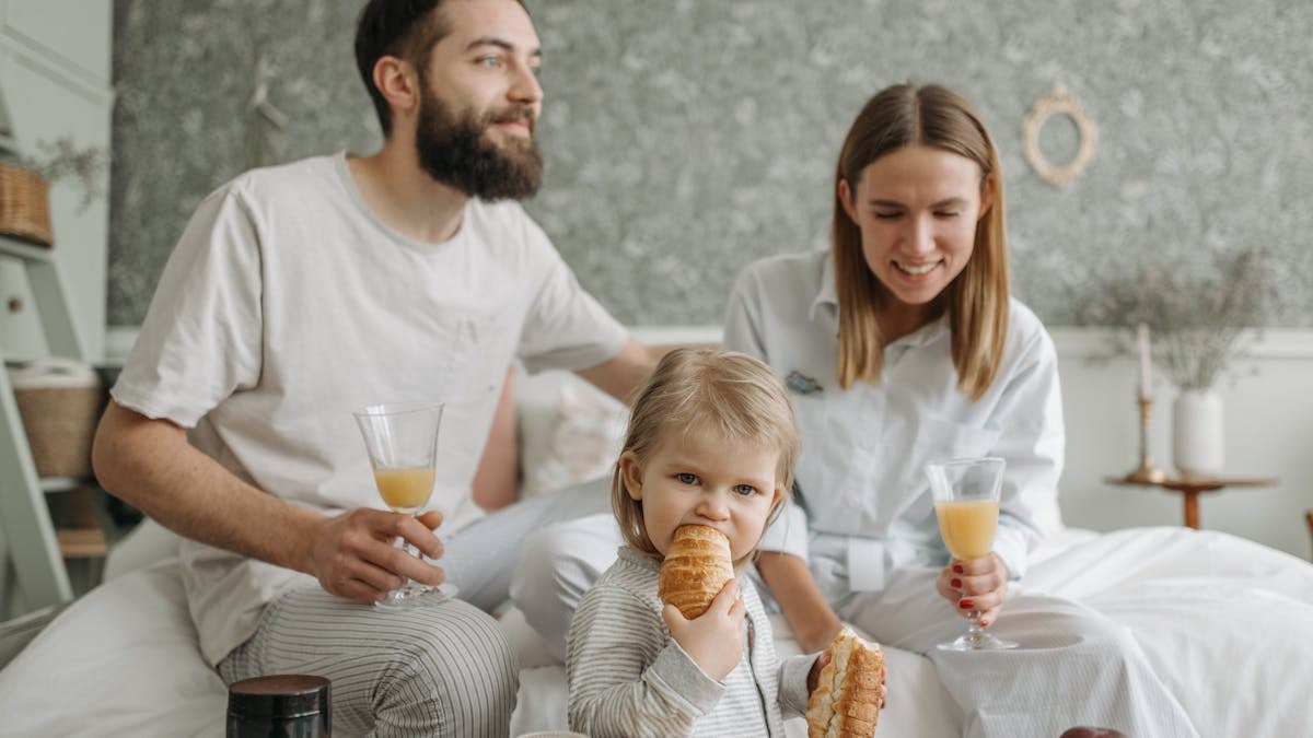 A family enjoying breakfast in their bedroom, featuring croissants and orange juice.