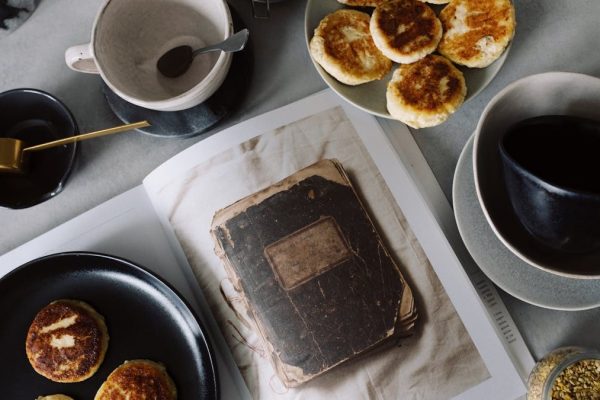Top view of plate with delicious curd pancakes placed on recipe book surrounded by various plates on gray tabletop in kitchen